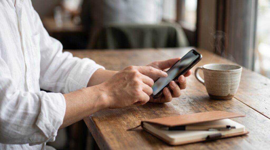 カフェのテーブルでスマートフォンとコーヒーカップが並ぶ手元のクローズアップ
